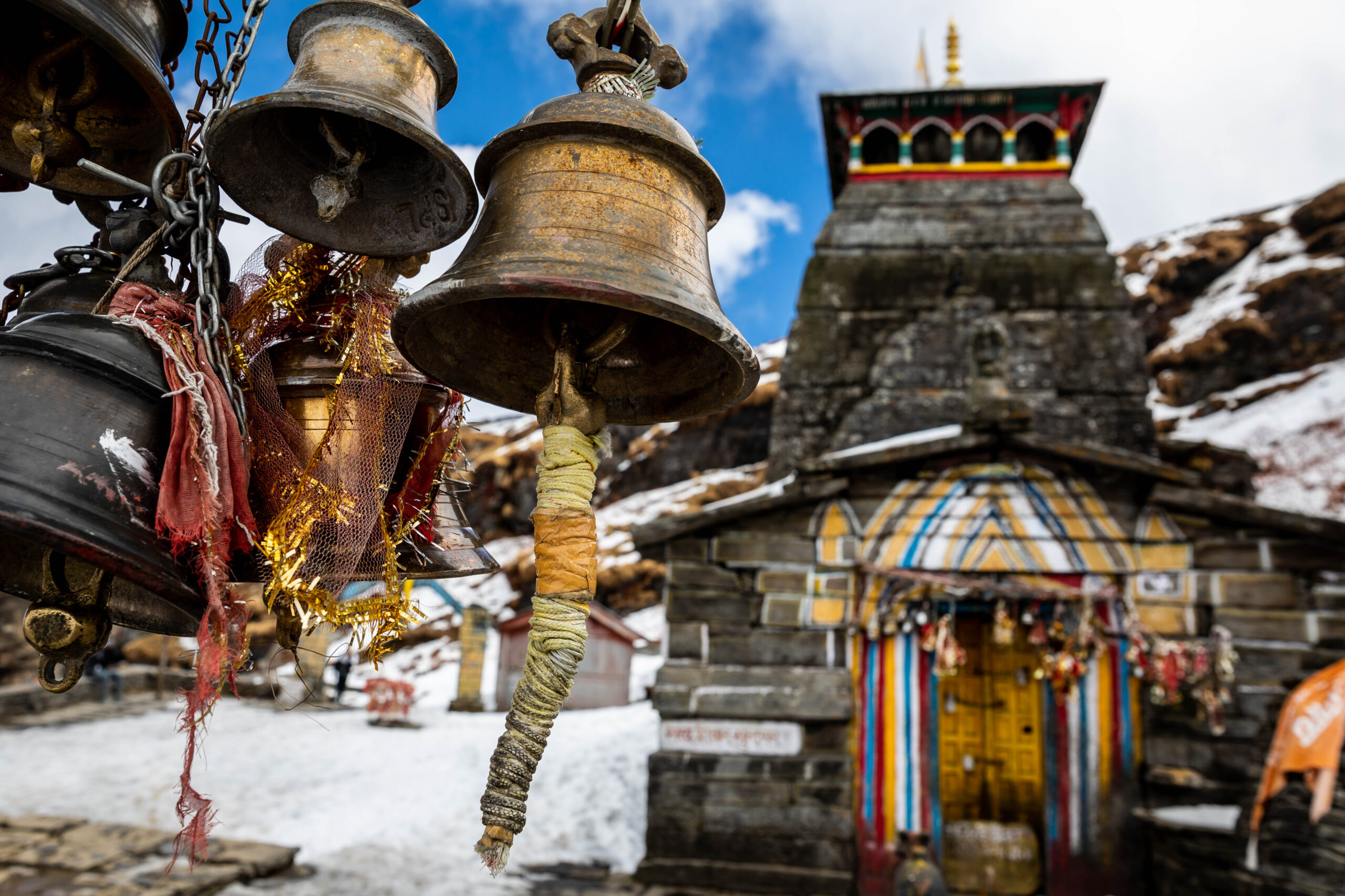 A snow-covered Himalayan temple adorned with large brass bells in the foreground, with a colorful entrance and prayer flags. This sacred site is part of The Himalayan Awakening: Spirituality, Nature & Impact tour.
