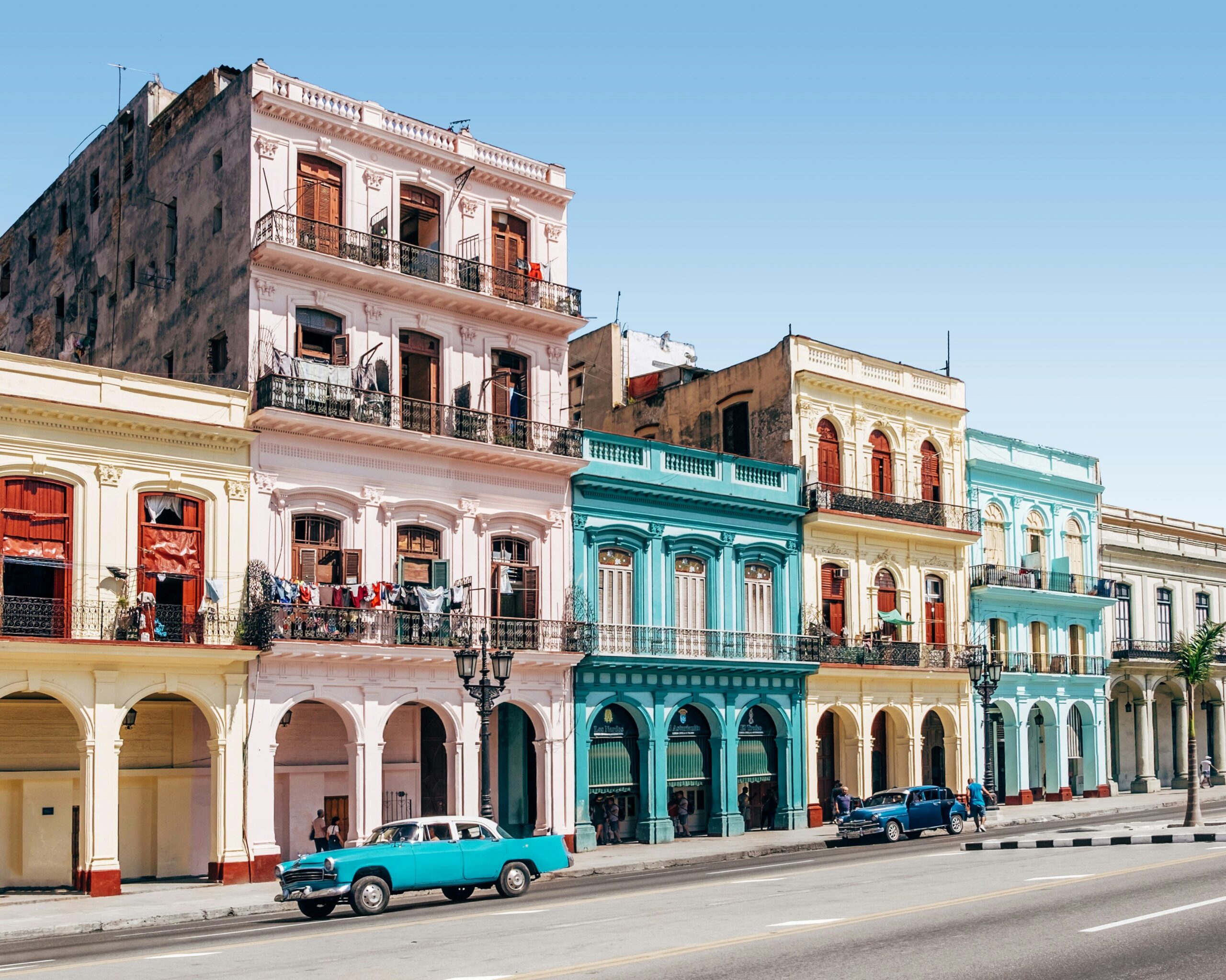 A vibrant view of Cuba's colorful streets, featuring pastel-hued buildings and a vintage car - Classic Cuba: Culture & Cuisine