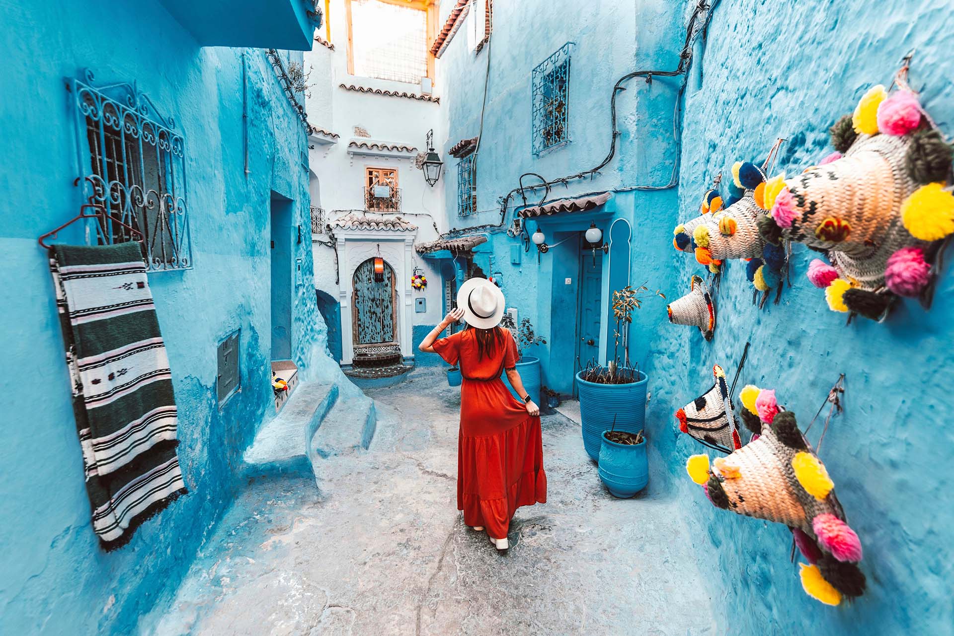 A woman in a vibrant red dress strolls through the picturesque streets of Chefchaouen - Wonders of Morocco - Sisterhood Travels