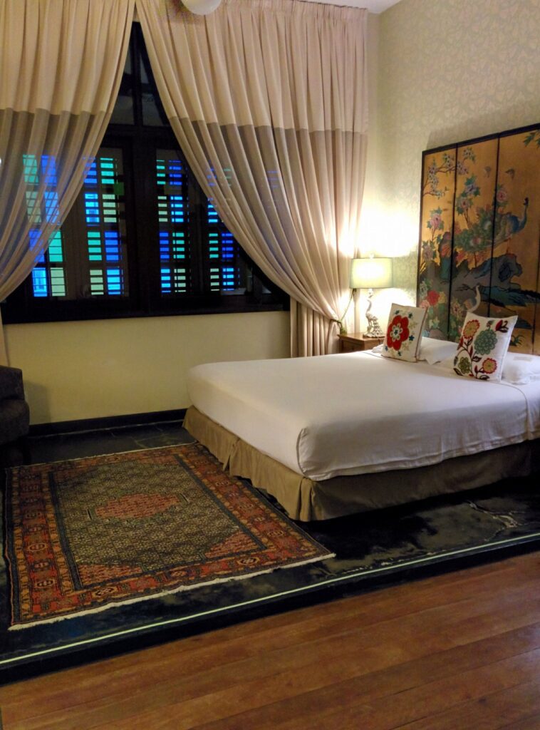 A simple room with beautiful rug and sheer curtains at the Campbell House Hotel Penang in George Town, Malaysia, recommended as a safe place for women to stay by JourneyWoman readers.